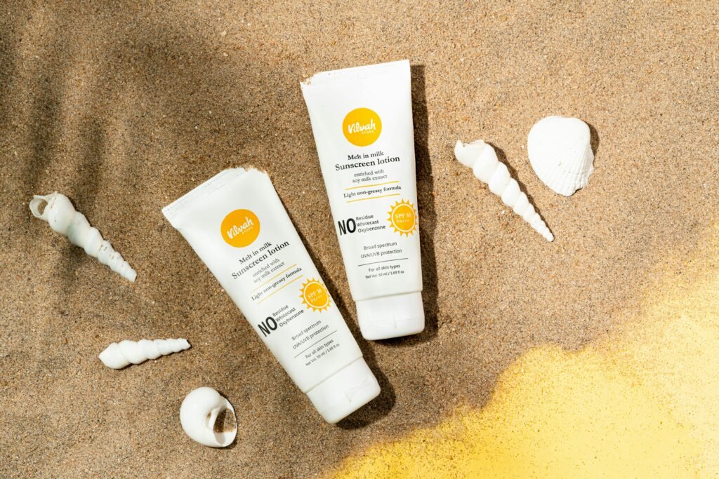 Two sunscreen lotion tubes on sandy beach alongside seashells for sun protection imagery.